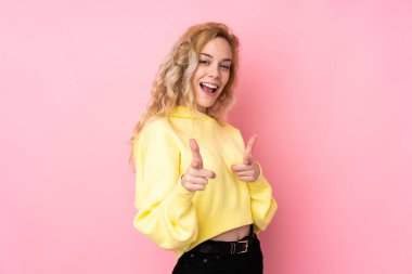 Pembe arka planda izole edilmiş eşofman üstü giyen genç sarışın kadın öne bakıyor ve gülümsüyor.