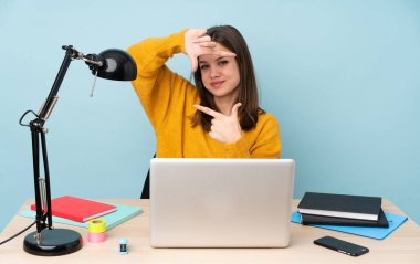 Öğrenci kız evinde çalışıyor. Mavi arka planda tek başına. Yüzüne odaklanıyor. Çerçeve sembolü