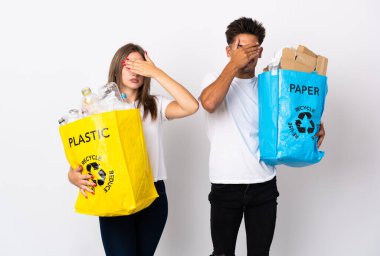 Plastik ve kağıt dolu bir çanta taşıyan genç çift, beyaz arka planda, gözleri elle kapatıyor. Bir şey görmek istemiyorum.