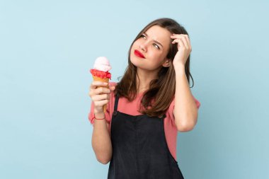 Kornet dondurması tutan genç bir kız mavi arka planda izole edilmiş şüpheleri var ve kafası karışmış bir yüz ifadesi var.