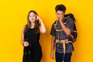 Sarı arka planda izole edilmiş büyük sırt çantalı genç dağcı çift mutsuz ve hayal kırıklığına uğramış.