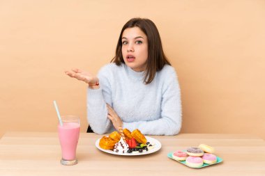 Bej arka planda izole edilmiş waffle yiyen genç kız şüphe uyandırıyor.