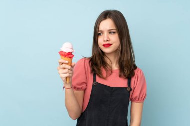 Kornet dondurması tutan genç kız üzgün bir ifadeyle mavi arka planda izole edilmiş.