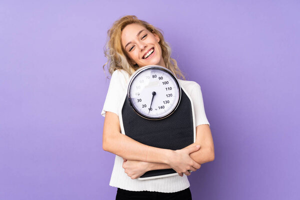 Young blonde woman isolated on purple background with weighing machine
