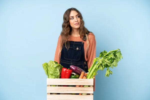 Farmer with freshly picked vegetables in a box making doubts gesture looking side