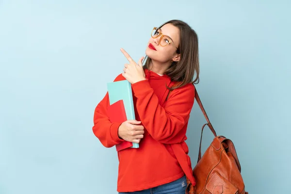 Student girl holding books isolated on blue background pointing with the index finger a great idea