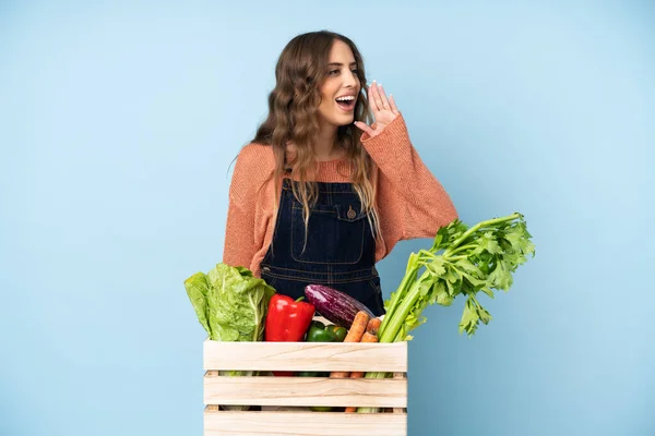 Farmer with freshly picked vegetables in a box shouting with mouth wide open to the lateral