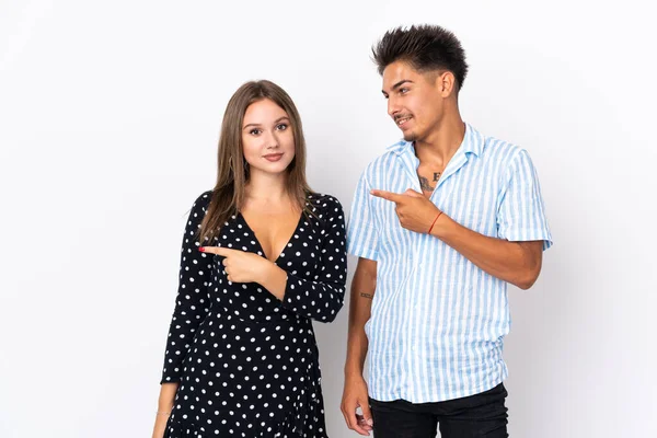 年轻的高加索夫妇在白色背景上被隔离 手指指向侧面并展示了一种产品 — 图库照片