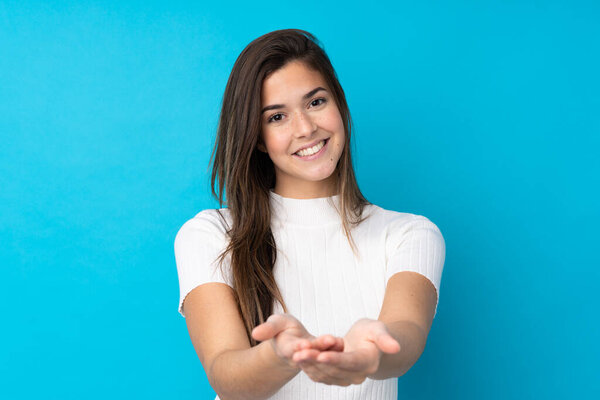 Девочка-подросток на изолированном синем фоне с воображаемым копирайтом на ладони, чтобы вставить объявление