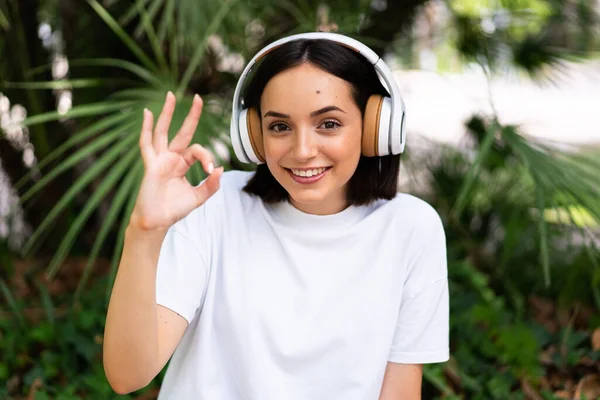 Mujer Joven Caucásica Con Auriculares Aire Libre Mostrando Signo Con —  Fotos de Stock