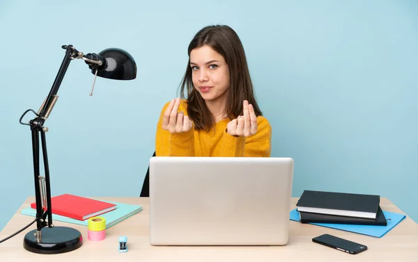 Student girl studying in her house isolated on blue background making money gesture