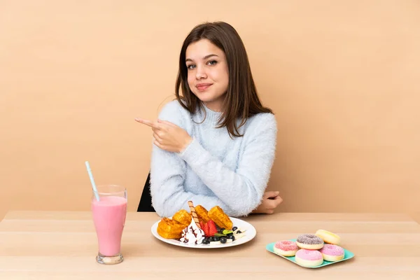 Chica Adolescente Comiendo Gofres Aislados Sobre Fondo Beige Apuntando Hacia —  Fotos de Stock