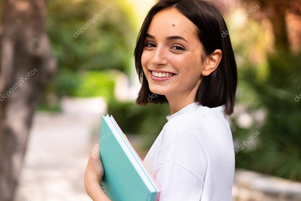 Young happy student woman holding notebooks at outdoors