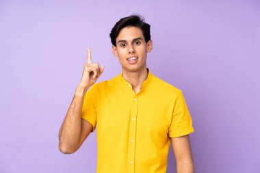 İzole edilmiş mor arka plandaki adam parmağını kaldırarak çözümü anlamaya çalışıyor.