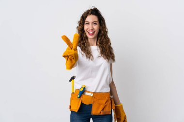 Beyaz arka planda izole edilmiş genç elektrikçi gülümsüyor ve zafer işareti gösteriyor.