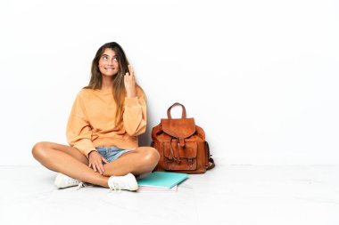 Genç bir kız öğrenci dizüstü bilgisayarla yerde oturuyor beyaz arka planda izole edilmiş ve şans diliyor.