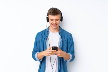 İzole edilmiş beyaz arka planı olan genç yakışıklı adam kulaklıklı cep telefonunu kullanıyor.