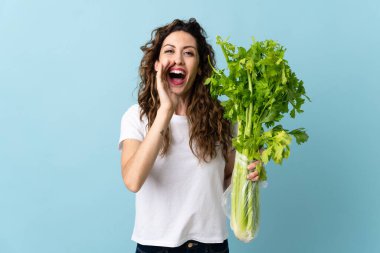 Mavi arka planda izole edilmiş bir kereviz tutan genç kadın ağzı açık bağırıyor.