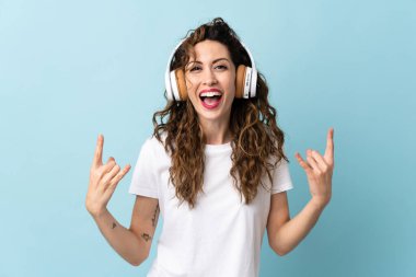 Kafkasyalı genç bir kadın mavi arka planda izole edilmiş rock hareketler yaparak müzik dinliyor.