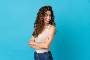 Mavi arka planda izole edilmiş, kolları bağlı ve mutlu genç beyaz bir kadın.