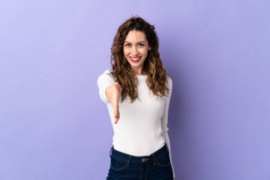 Mor arka planda izole edilmiş genç beyaz kadın iyi bir anlaşma için el sıkışıyor.