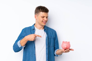 Soyutlanmış beyaz arka planı olan yakışıklı genç bir adam elinde büyük bir kumbara tutuyor.