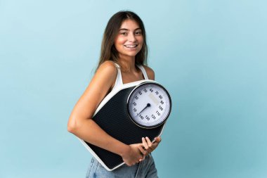 Genç beyaz kadın, mavi arka planda, tartı makinesiyle izole edilmiş.