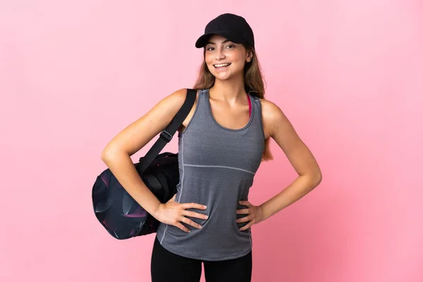 Young sport woman with sport bag isolated on pink background posing with arms at hip and smiling