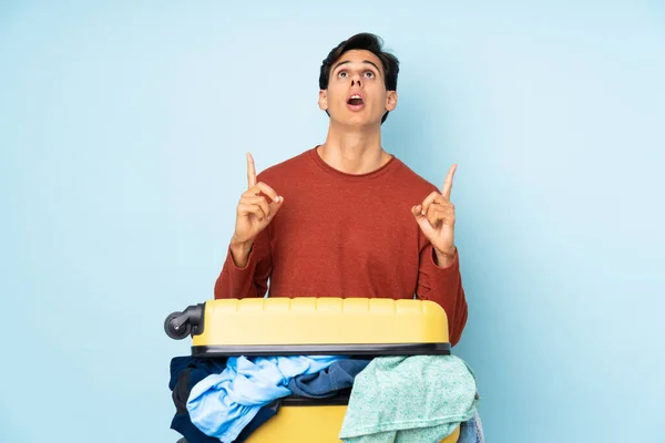 Man with a suitcase full of clothes over isolated blue background pointing with the index finger a great idea