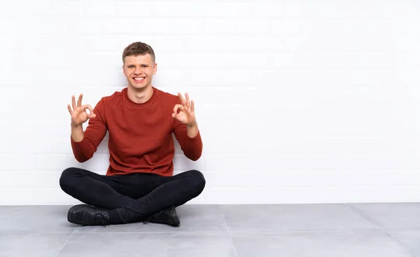Mladý Pohledný Muž Sedící Podlaze Ukazující Znamení Prsty — Stock fotografie