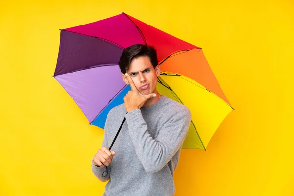 Man holding an umbrella over isolated yellow background thinking an idea