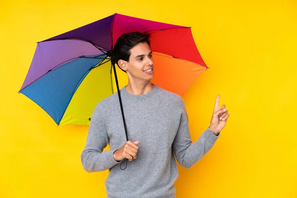 Muž Držící Deštník Nad Izolovaným Žlutým Pozadím Ukazující Prstem Stranu — Stock fotografie