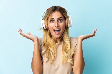 Genç sarışın Uruguaylı, mavi arka planda izole edilmiş şaşırmış ve müzik dinliyor.