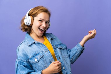 Genç Gürcü kadın mor arka planda izole edilmiş müzik dinliyor ve gitar hareketi yapıyor.