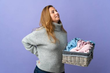 Mor arka planda bir çamaşır sepetini tutan orta yaşlı kadın gayret gösterdiği için sırt ağrısından muzdarip.