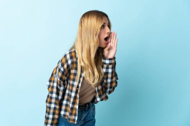 Genç sarışın Uruguaylı, mavi arka planda izole edilmiş ve ağzı sonuna kadar açık bağırıyor.