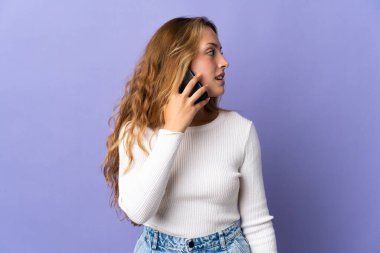 Mor arka planda izole edilmiş genç sarışın bir kadın cep telefonuyla sohbet ediyor.