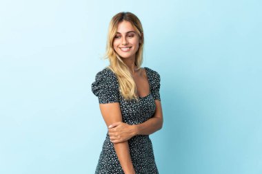 Genç sarışın Uruguaylı, mavi arka planda tek başına gülüyor.