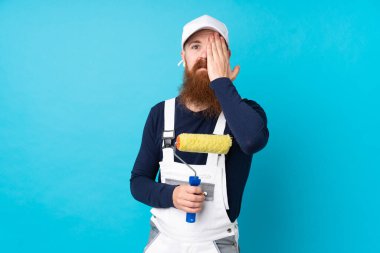 Uzun sakallı bir ressam, mavi arka planda, bir gözü elle kapatıyor.