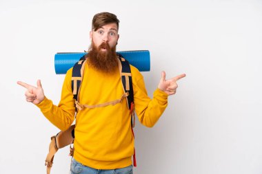 İzole edilmiş beyaz arka planı olan büyük bir sırt çantasıyla dağcı genç adam yan taraftakilerin şüphelerini işaret ediyor.