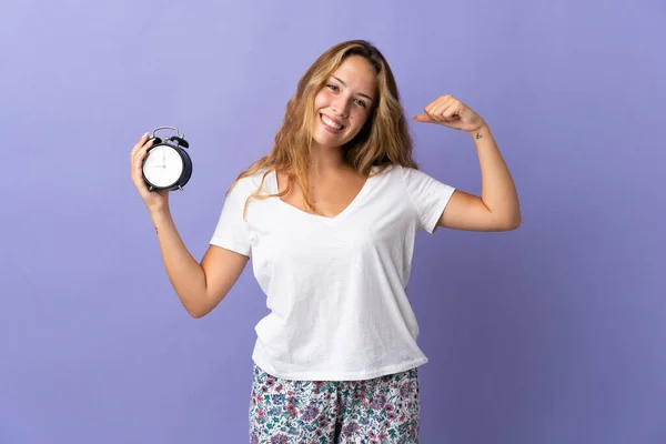 Giovane Donna Bionda Isolata Sfondo Viola Pigiama Tenendo Orologio Mentre — Foto Stock