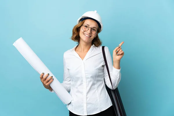 Young architect Georgian woman with helmet and holding blueprints over isolated background showing and lifting a finger in sign of the best