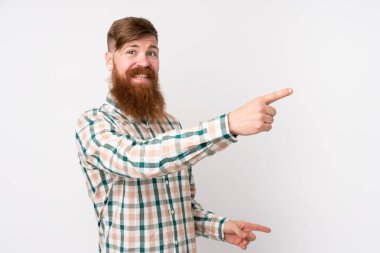 Uzun sakallı, soyutlanmış beyaz arkaplanı olan kızıl saçlı bir adam, parmağını kenarı gösteriyor ve bir ürün sunuyor.