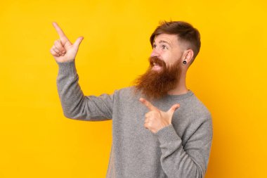 İzole edilmiş sarı arka planı olan uzun sakallı kızıl saçlı adam işaret parmağıyla işaret ediyor. Harika bir fikir.
