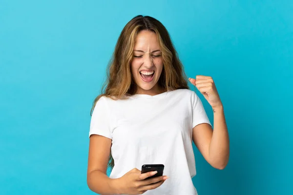 Junge Blonde Frau Isoliert Auf Blauem Hintergrund Mit Handy Siegerposition — Stockfoto