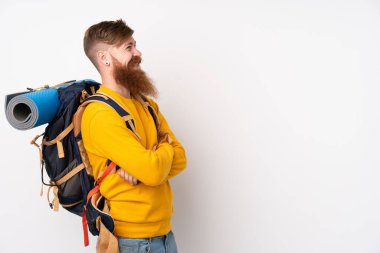 İzole edilmiş beyaz arka plan üzerinde büyük bir sırt çantası olan genç dağcı yan tarafa bakıyor.