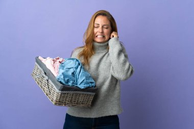 Mor arka planda izole edilmiş çamaşır sepetini tutan orta yaşlı kadın hayal kırıklığına uğramış ve kulaklarını kapatmış.
