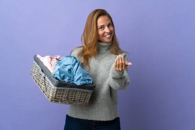 Mor arka planda izole edilmiş çamaşır sepetini tutan orta yaşlı bir kadın benimle gelmesi için davet ediyor. Gelmene sevindim.