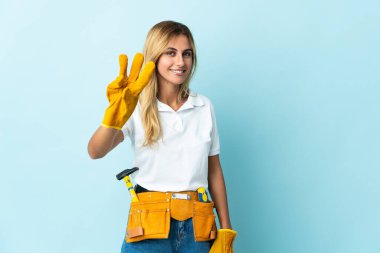 Genç sarışın Uruguaylı elektrikçi kadın mavi arka planda izole edilmiş mutlu ve parmaklarıyla üçe kadar sayıyor.