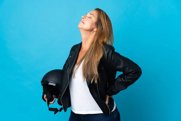 中世の女性は努力をしたために腰痛に苦しむ青い背景に隔離されたオートバイのヘルメットを持っている — ストック写真